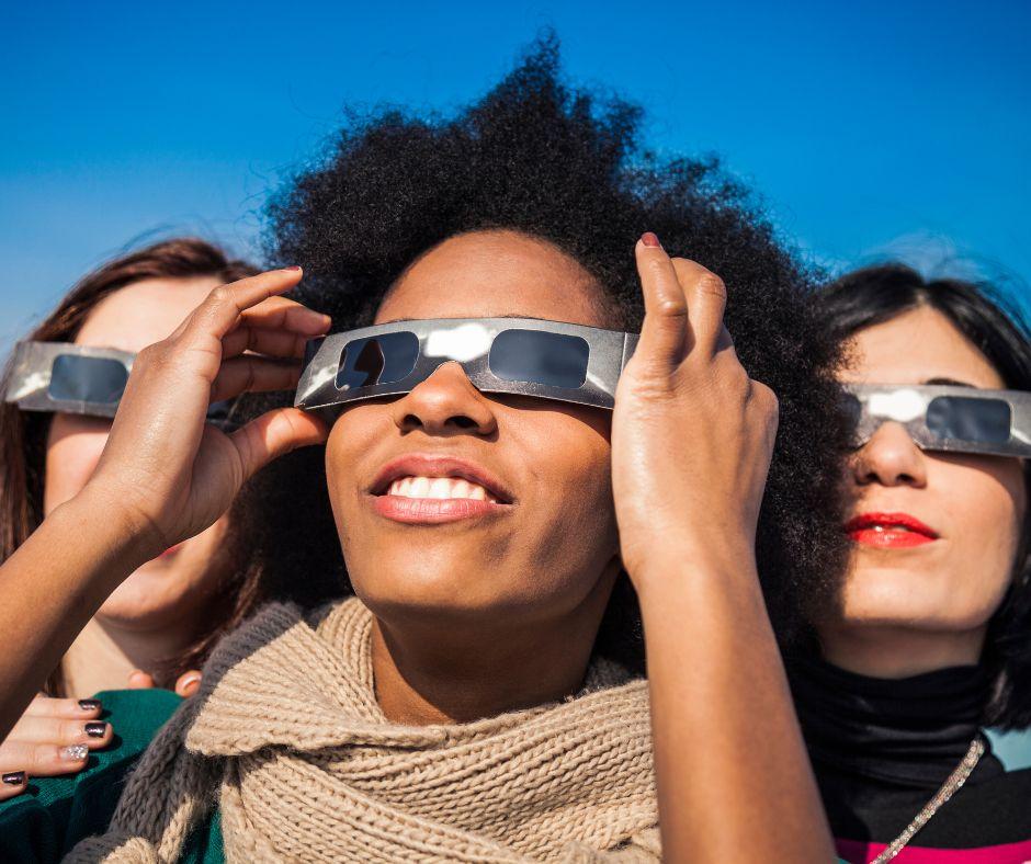 Three women wearing protective glasses viewing an eclipse