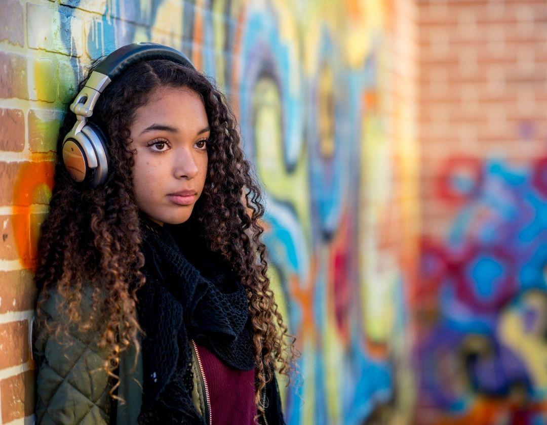 A bored teenager resting against a wall with graffiti on it