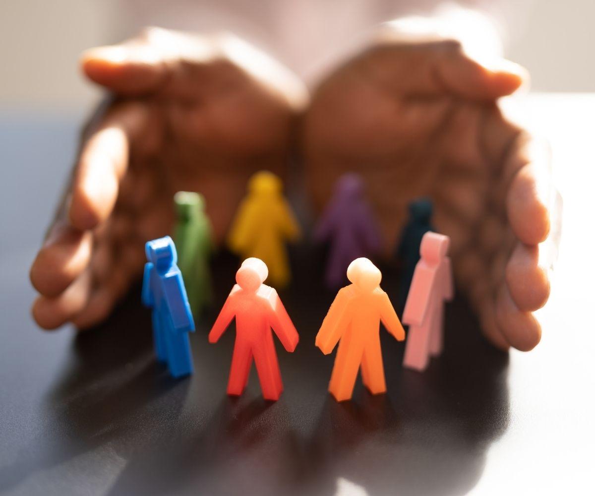 A pair of hands enveloping small rainbow colored toy people